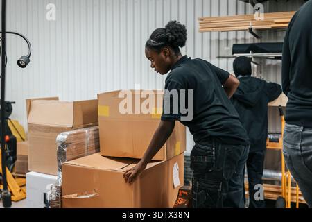 Female warehouse worker keeping cardboard boxes on hand truck in factory Stock Photo