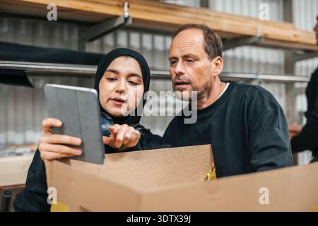 Female worker using tablet PC while discussing with male coworker in warehouse Stock Photo