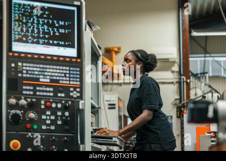 Focused young female metal worker operating machine in factory Stock Photo