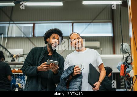 Male workers looking away while discussing with each other in metal factory Stock Photo