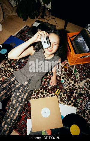 High angle view of woman looking through vintage camera while reclining on carpet at home Stock Photo