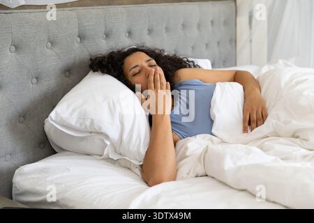 White duvet and pillows are resting on bed against tufted gray headboard near sheer curtain Stock Photo