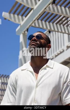 Mature African American man wearing white shirt and round sunglasses looking up under pergola Stock Photo