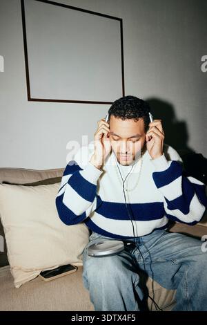Young man listening to music through personal stereo while sitting on sofa at home Stock Photo