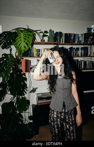 Smiling young woman photographing through old film camera while standing at home Stock Photo