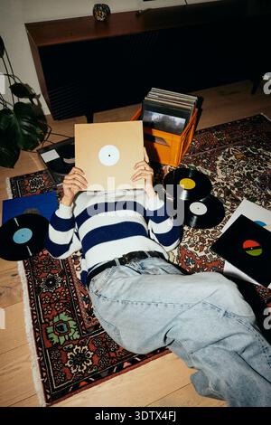 High angle view of young man covering face with vinyl cover while lying down on carpet at home Stock Photo
