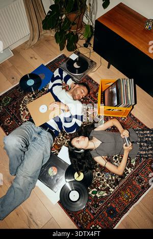 High angle view of young friends lying down on carpet with record vinyls at home Stock Photo