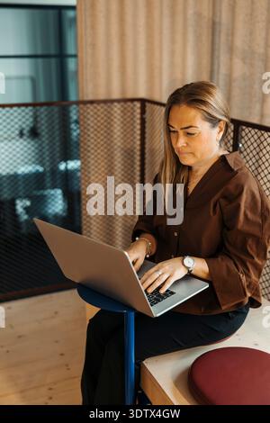 Mature female entrepreneur using laptop while sitting and working at modern office Stock Photo