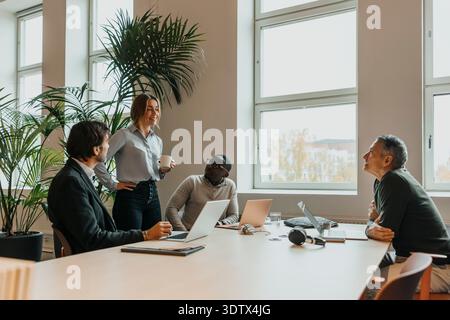 Smiling businesswoman sharing marketing ideas with male colleagues sitting around desk in office Stock Photo
