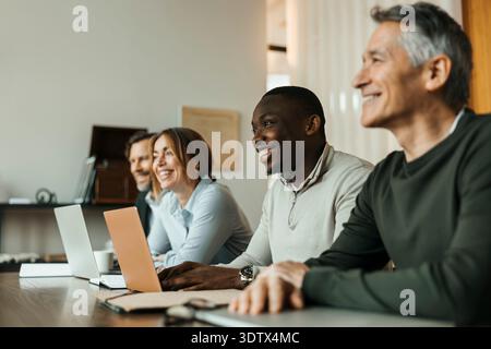Happy male and female entrepreneurs sitting with laptops on table in meeting room Stock Photo