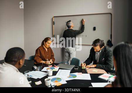 Rear view of senior businessman writing on whiteboard in team meeting at office Stock Photo