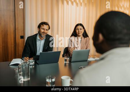 Smiling male and female entrepreneurs taking interview of candidate in office board room Stock Photo