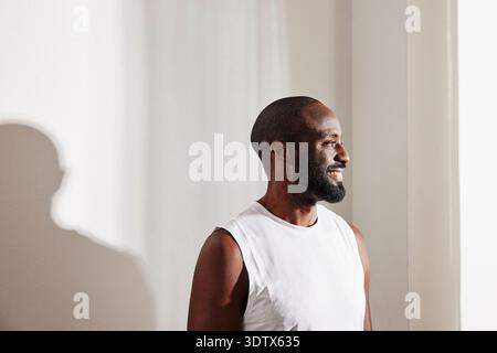 Smiling man looking away while standing in front of wall at home Stock Photo