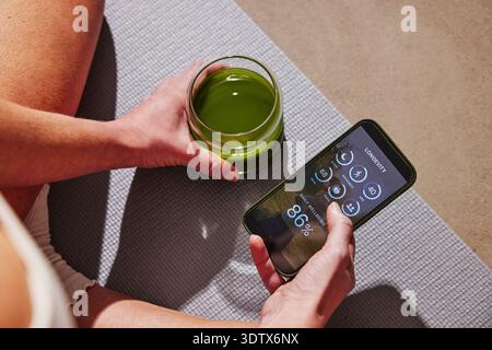 High angle view of woman examining body scan health data on smart phone while sitting with detox juice Stock Photo