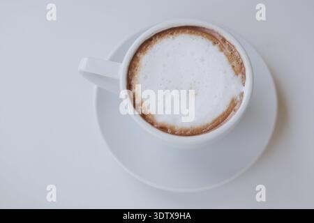 Coffee sits in a white cup on a plain table Stock Photo