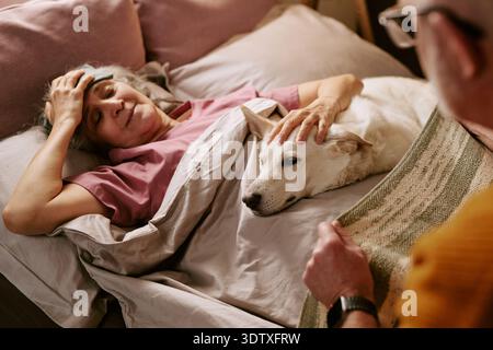 Senior Caucasian Woman Lying in Bed Comforted by Dog and Senior Man Stock Photo