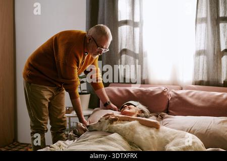 Senior Caucasian Man Comforting Senior Caucasian Woman Resting in Bed Stock Photo