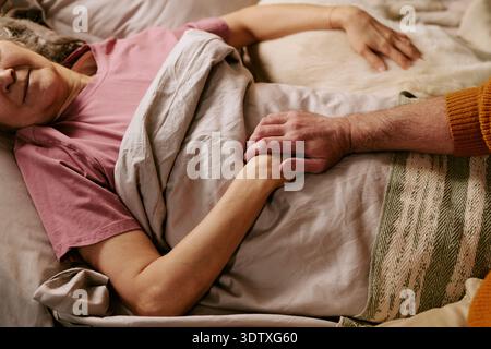 Senior Caucasian Woman Lying in Bed Holding Hands with Senior Man Stock Photo