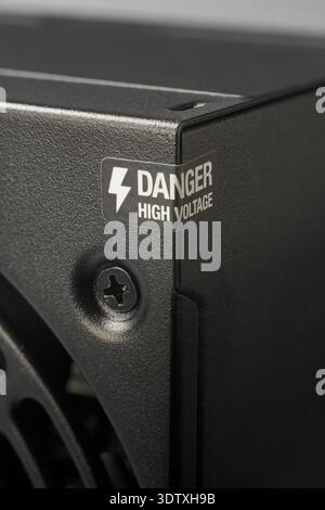danger high voltage sticker on computer power supply isolated neutral background, warning label wrapped around metallic casing corner, textured black Stock Photo