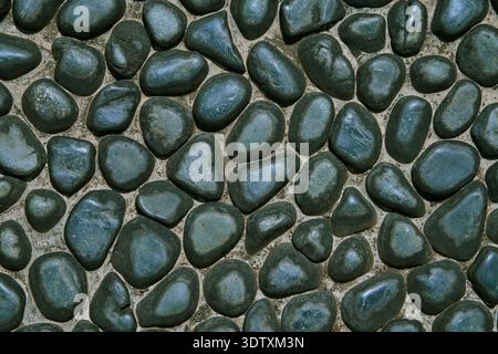 Dark blue-black river pebbles embedded in a concrete or mortar surface. The stones are rounded and polished, creating a natural mosaic texture. Stock Photo
