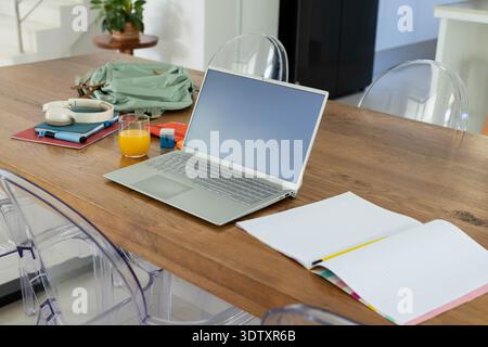 Silver laptop sitting open on wooden dining table with lined notebook and yellow pencil nearby Stock Photo