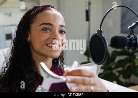 African American woman wearing maroon top holding metal tool and using boom mic on couch Stock Photo
