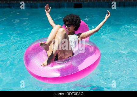 Bright pink inflatable ring with backrest is floating in clear blue pool, sunlight glinting Stock Photo