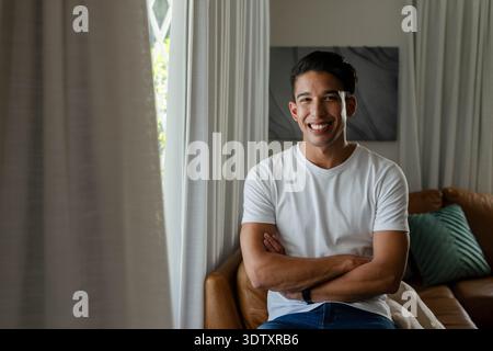African American man sitting on brown leather sofa, wearing white t-shirt and blue jeans, smiling Stock Photo