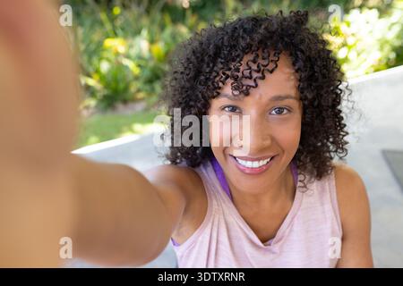 African American woman taking selfie on patio holding phone, wearing pink top with sports bra strap Stock Photo