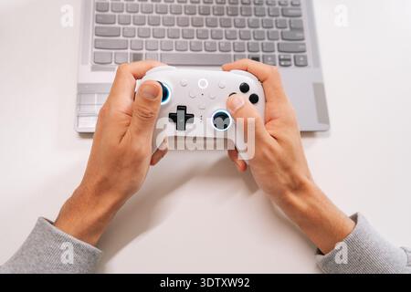 Cropped shot of skilled gamer male holding gamepad, streaming online video game on laptop, enjoying recreation and digital entertainment at home Stock Photo