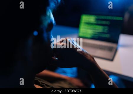 Pensive developer writing code late at night, working on programming software, debugging system issues, ensuring cyber security protection during dark Stock Photo