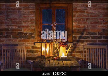 Still life with candles on a table, chairs next to it, it's getting dark outside, cozy atmosphere at dusk, winter evening Stock Photo