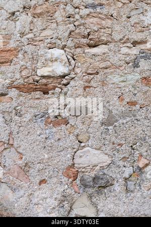 A high-resolution close-up of an ancient stone wall. It features a rustic mix of weathered earth-toned rocks, fragments of red brick, and coarse sandy Stock Photo