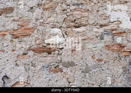 A high-resolution close-up of an ancient stone wall. It features a rustic mix of weathered earth-toned rocks, fragments of red brick, and coarse sandy Stock Photo
