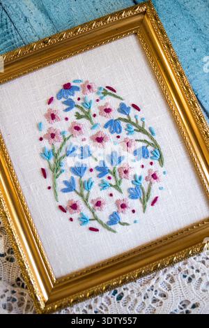 Framed floral hand embroidery on linen fabric placed on rustic blue wooden background with threads, scissors and lace. Flat lay craft composition Stock Photo