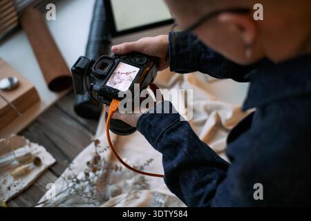 Caucasian young adult man holding digital camera, photographing flat lay arrangement on table, focusing on creative composition, hands and camera visible, workspace setting Stock Photo