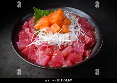 A Japanese rice bowl topped with diced tuna, fresh salmon sashimi, and shredded daikon radish, served in a dark ceramic bowl on a moody background. Stock Photo