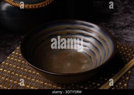 A Japanese ceramic bowl and teapot set displayed on a bamboo mat under moody lighting. The setup captures traditional Japanese tableware elegance. Stock Photo