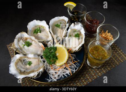 A platter of fresh oysters served on shredded daikon with assorted condiments, including seafood sauce, fried shallots, and chili paste Stock Photo