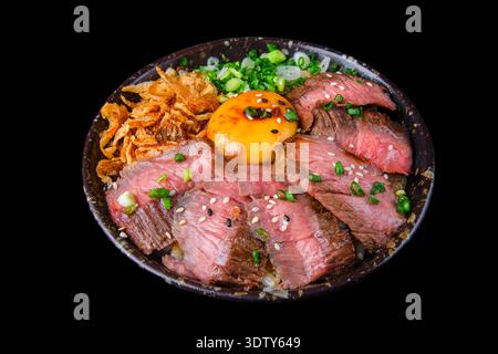 Grilled beef slices served on a rice bowl, topped with raw egg yolk and kimchi, offering a rich and flavorful Japanese dish. Isolated on a black background Stock Photo
