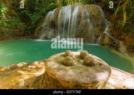 A rounded stone platform sits beside a turquoise freshwater pool at the base of a small forest waterfall. Stock Photo