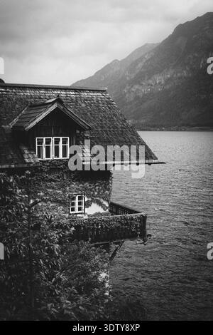 Black and white view of a historic house on a lake with mountains in the background Stock Photo
