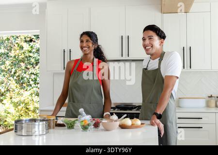 African American couple wearing olive-green aprons chopping onions on kitchen island with steamer Stock Photo