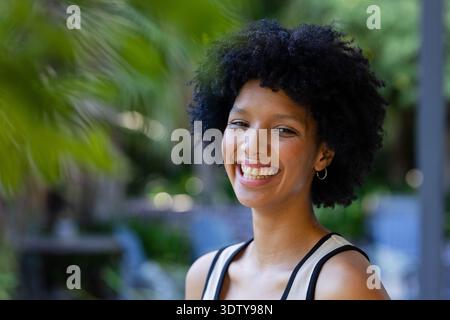 African American woman smiling in garden with palm leaves, in black-strap top and hoop earrings Stock Photo