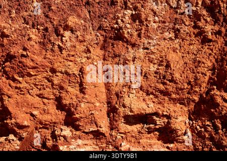 Full frame background texture of dry red clay soil and rough earth cliff surface. Stock Photo