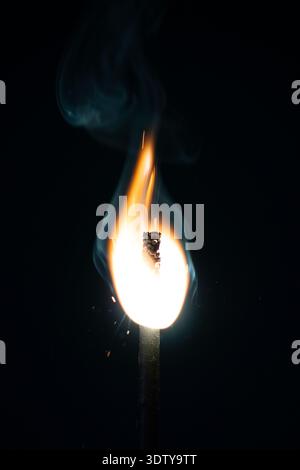Close-up of a burning Bengal match with bright flame, glowing tip, sparks and rising smoke against a dark background. Stock Photo