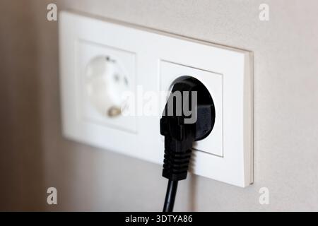 Black power plug connected to white wall socket, home electricity concept Stock Photo