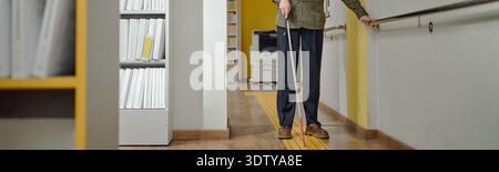 Blind Man Navigating Library Hallway Using Cane and Guide Rail Stock Photo