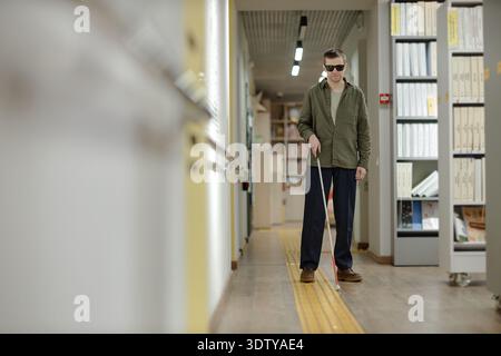 Young Adult Man Navigating Library Corridor Using Cane Independently Stock Photo