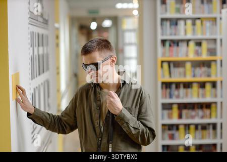 Young Man Navigating Library Using Tactile Guide and Cane Stock Photo